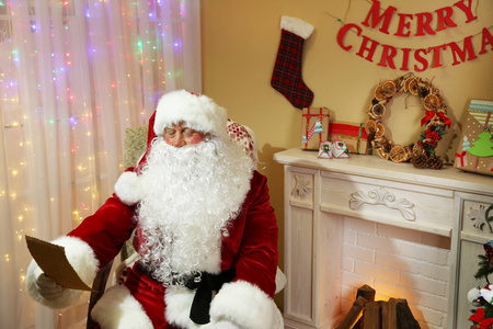 圣诞老人坐在舒适的椅子上，在家里壁炉旁的礼物列表