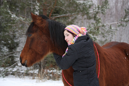 美丽少女在冬季中拥抱匹棕色的马
