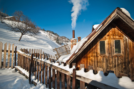 旧的木制平房与山被在背景中的雪覆盖着。在山景观的明亮寒冷的冬天里。喀尔巴阡山，罗马尼亚。被雪覆盖着的孤立木山的房子小木屋小屋