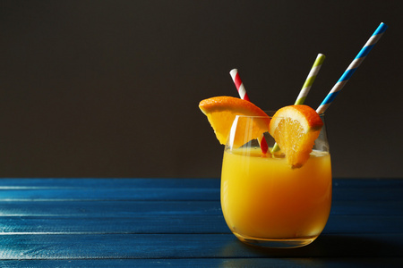 杯橙汁与秸秆和片上颜色木桌子上，在黑暗的背景