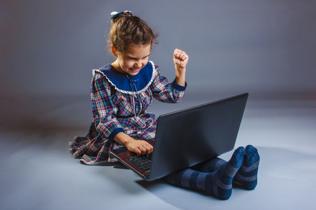 女孩子姿态是坐玩笔记本电脑在灰色的背景