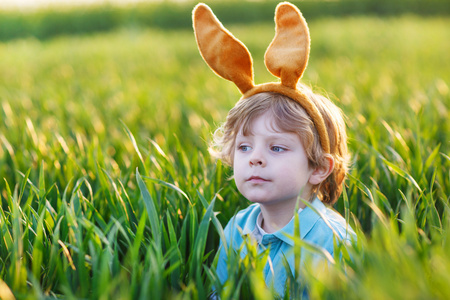 玩在绿草的复活节兔子耳朵的可爱孩子
