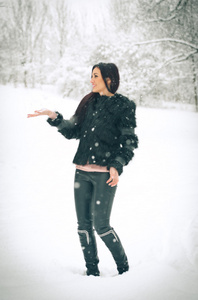 快乐的黑发女孩玩雪冬季景观中的视图。美丽的年轻女性在冬天背景。年轻漂亮的女人，在室外的一个冬日温暖柔软的衣服
