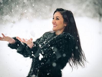 快乐的黑发女孩玩雪冬季景观中的视图。美丽的年轻女性在冬天背景。年轻漂亮的女人，在室外的一个冬日温暖柔软的衣服