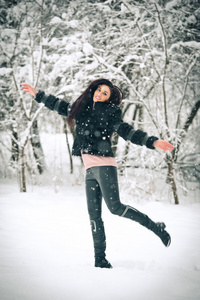 快乐的黑发女孩玩雪冬季景观中的视图。美丽的年轻女性在冬天背景。年轻漂亮的女人，在室外的一个冬日温暖柔软的衣服