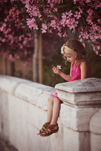 美丽的小女孩下粉红色棵开花的树墙上坐在夏季的一天