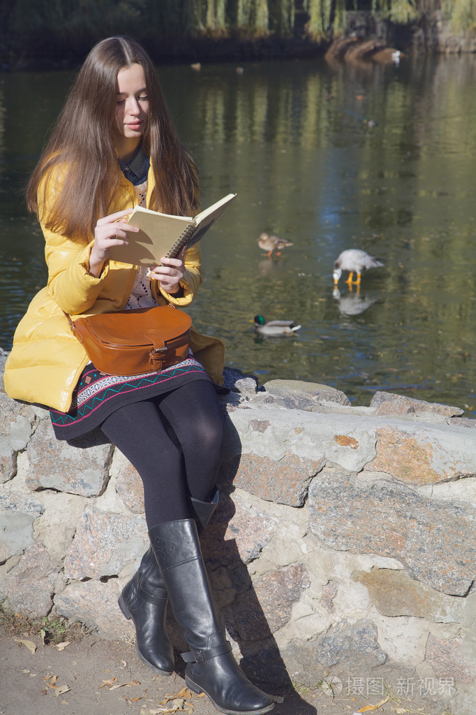 漂亮的女生坐在市池塘在太阳附近的栏杆上