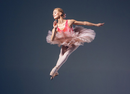 美丽的女芭蕾舞演员在灰色的背景上。芭蕾舞女演员穿着粉红色的短裙和普安特鞋