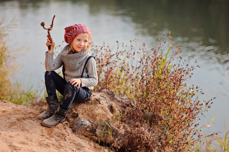 可爱的孩子小女孩微笑着坐在一起贴在江边的沙滩上的粉红色针织帽子