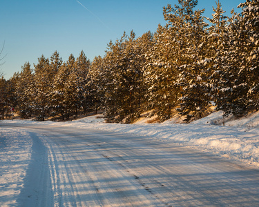 美丽的冬天路穿过白雪覆盖的田地，日落和森林