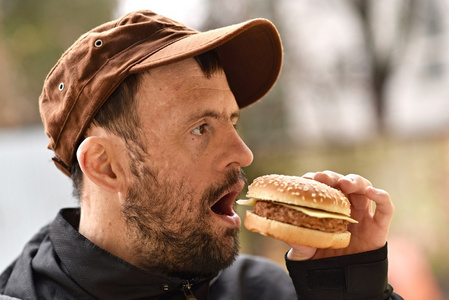 汉堡男子吃一个汉堡包一个年轻男子吃汉堡包和工作在笔记本电脑的肖像