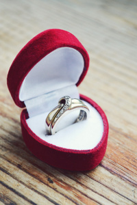 红色心形戒指盒木制的桌子上的白金订婚戒指。