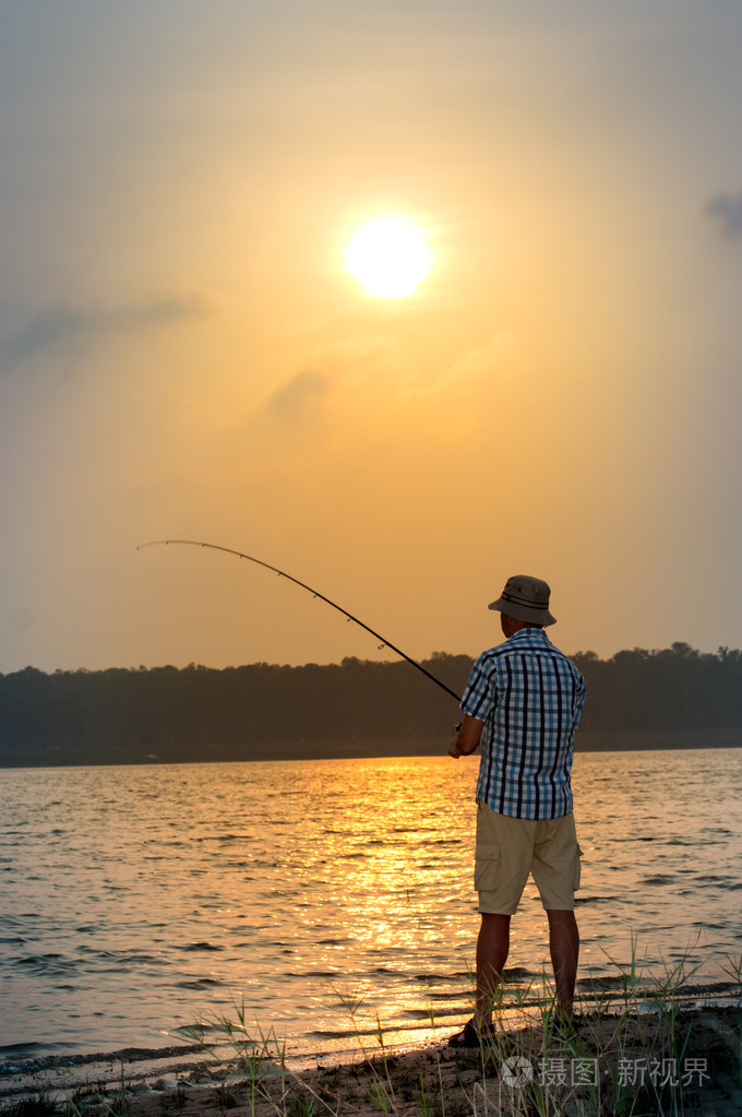 年轻人在日落时从岸边钓鱼