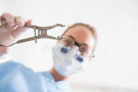 戴着口罩的牙医拿着钳子捂住病人
