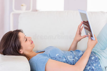 漂亮的黑发女人在沙发上用她的平板电脑