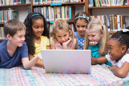 可爱的小学生在图书馆看笔记本电脑
