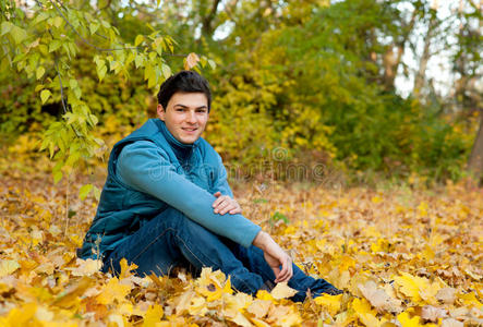 年轻的微笑男子在秋天公园放松。