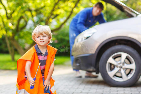 在父亲修理家用汽车时，穿着橙色安全背心的小男孩