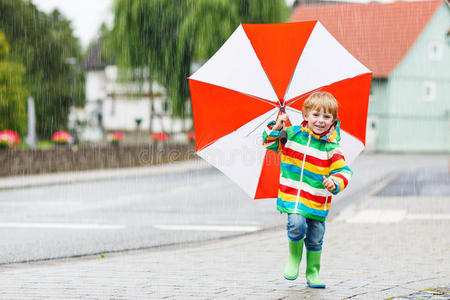 漂亮的孩子带着红色的雨伞和五颜六色的夹克在户外