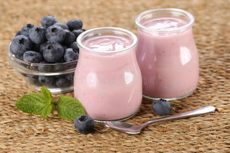 玻璃罐里放着蓝莓酸奶，垫子上的玻璃碗里放着蓝莓