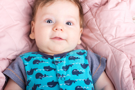 可爱的小宝宝一张粉红色的床。一个婴儿的画像。一个微笑的孩子的肖像。白色的床上的孩子。英俊的男孩