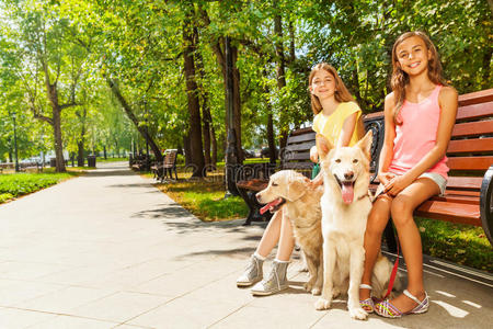 两个带着狗的女孩坐在公园的长凳上
