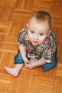室内的一个可爱的男婴，坐在家里的木地板上的肖像
