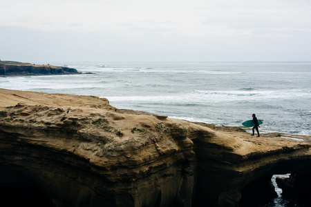 冲浪者在沿太平洋在日落悬崖悬崖上行走