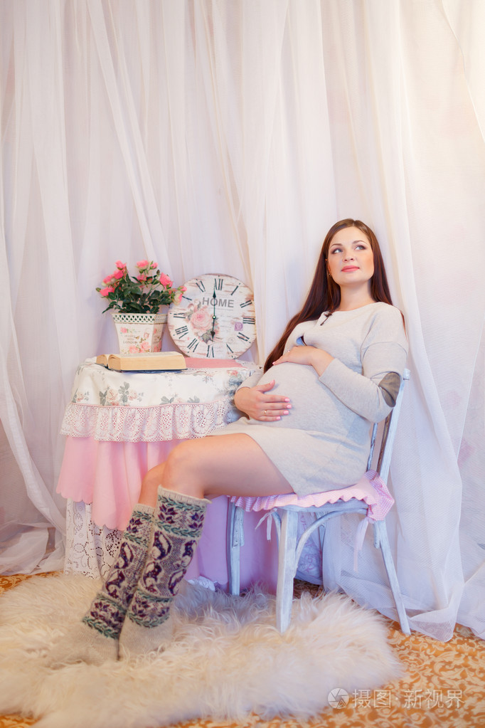 美丽的孕妇坐在一把椅子上抱着她的肚子
