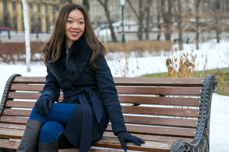 幸福的亚洲女人在冬季公园的长椅上
