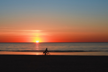 日落海滩上一个骑自行车的剪影