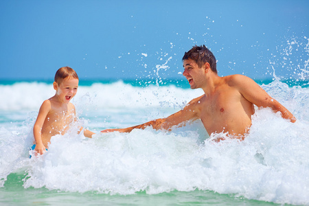 快乐的父亲和儿子跳跃的波浪，暑假中