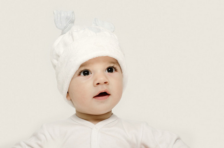 天真的孩子戴着白色的帽子，看起来很可爱。孩子穿的冬天，可爱的新生儿。可爱的宝宝画像看好奇。宝宝打扮成有趣的兔子，戴着白色帽子的兔