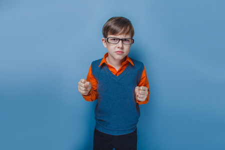 欧洲人的小男孩的眼镜皱着眉头，不开心的节目拳头在蓝色背景上的十年
