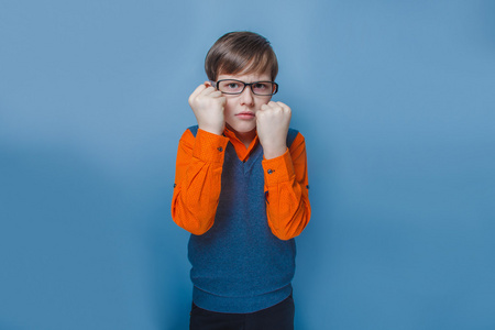 欧洲人的小男孩的眼镜皱着眉头，不开心的节目拳头在蓝色背景上的十年