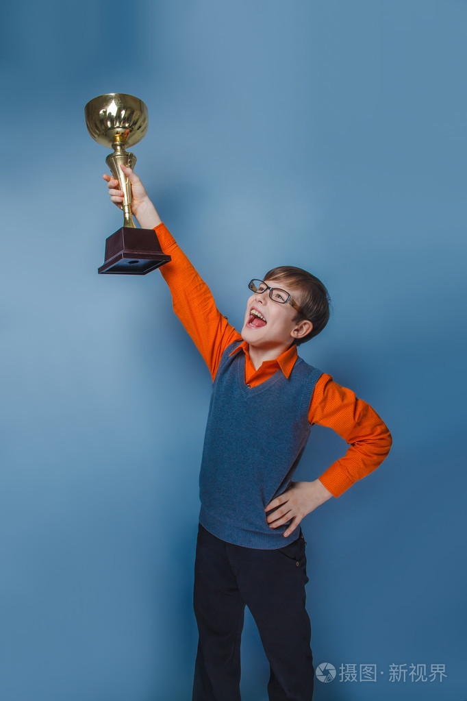 欧洲人的小男孩的十年中持有杯奖在蓝色背景上的眼镜