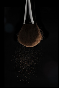 垂直的特写照片的化妆刷与米色粉在黑色背景上孤立的议案