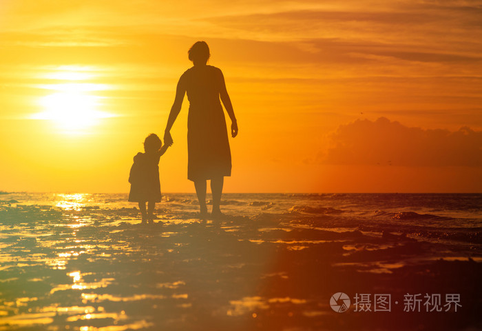 母亲和小女儿在日落时在海滩上行走