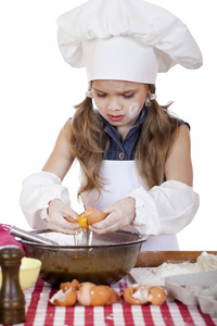 在一条白色的围裙的小厨师女孩打破鸡蛋深碟内