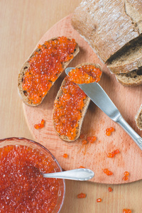红鱼子酱碰杯三明治用银刀，碗勺子与新鲜美味红鱼子酱烤木桌背景上的自制健康面包