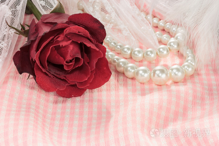 特写红玫瑰与珍珠项链上粉红色织物背景