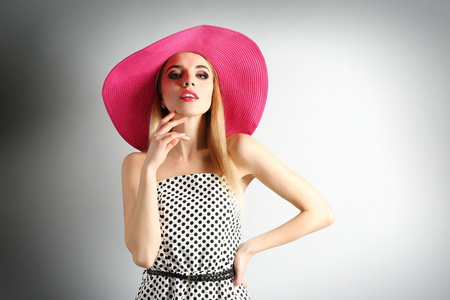 在灰色的背景上的粉红色帽子表达年轻模型