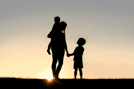 母亲和年幼的孩子，手牵着手在日落时的剪影