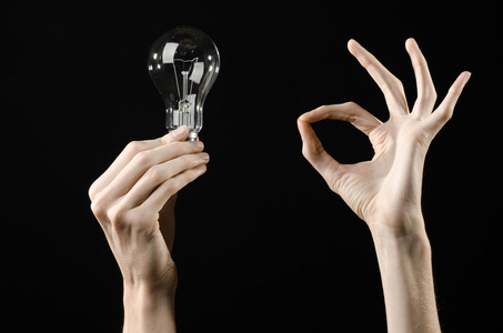 能源消费和节能主题 人类的手一个灯泡在工作室中的黑色背景上