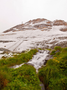 阿尔卑斯山旅游区的第一场雪。有急流小溪的新鲜绿色草地。背景是阿尔卑斯山脉的山峰。