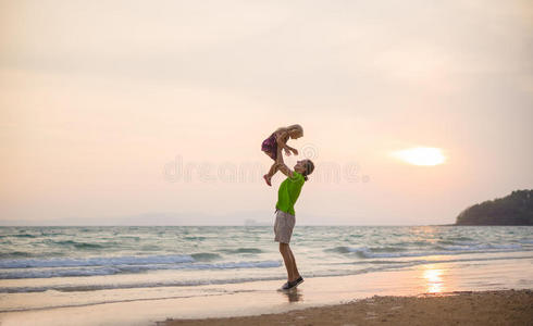 父亲背着游艇，在日落海滩上用手托起女儿