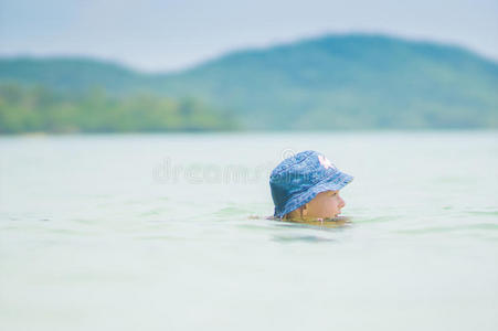 可爱的蓝帽子女孩在海滩附近的海洋里游泳