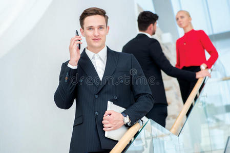 商人在和客户打电话。年轻的商人站在台阶上，拿着平板电脑，而他的同事们