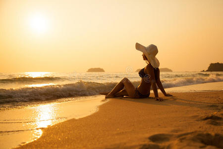 日落时热带海滩上戴草帽的年轻女孩。夏天