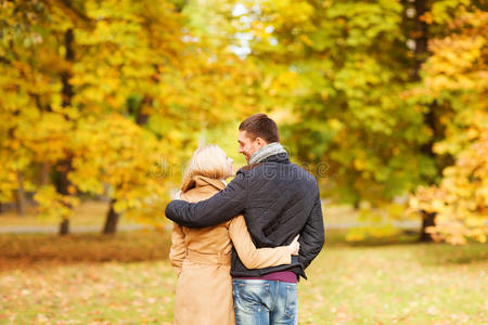 一对微笑的情侣从后面拥抱在秋天的公园里